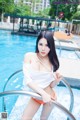 A woman in a white top and orange bikini posing by a pool.