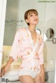 A woman in a pink robe standing in a bathroom.