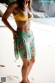 A woman in a yellow bikini top and green shorts on the beach.