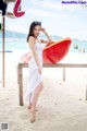 A woman in a white dress standing on a beach next to a red boat.