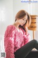 A woman sitting on a chair wearing a pink fuzzy sweater.