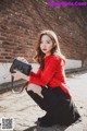 A woman in a red sweater and black skirt crouching down with a handbag.