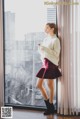 A woman standing in front of a window looking at her phone.