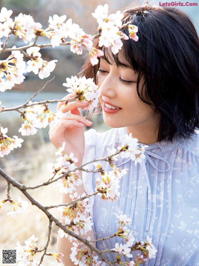 A woman in a blue dress standing next to a tree with white flowers.