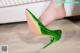 A woman wearing a pair of green high heels on a wooden floor.