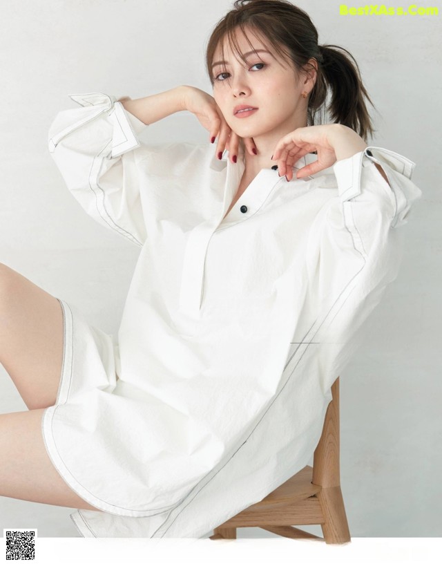 A woman sitting on a chair wearing a white shirt dress.