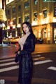 A woman in a black leather coat standing on a city street at night.