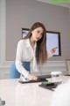 A woman in a white shirt and blue skirt standing at a desk.