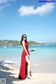 A woman in a red dress standing on a beach.