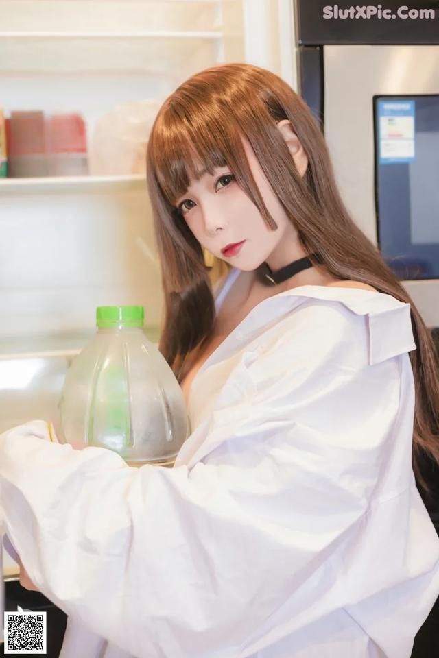 A woman holding a bottle of water in front of a refrigerator.