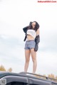 A woman standing on top of a car with her hands on her head.