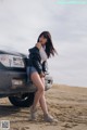 A woman standing next to a car on a beach.