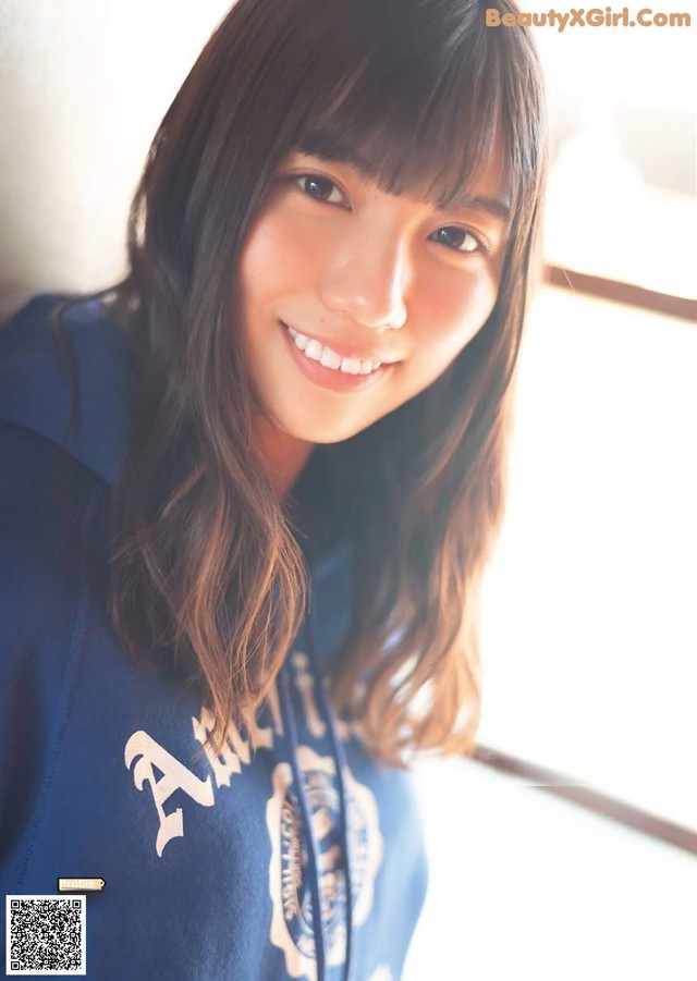 A young woman in a blue sweatshirt smiles at the camera.