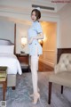 A woman in a blue shirt and white stockings posing in a hotel room.